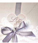 <p>Invitație de nuntă din carton crem care se pliază în trei părți formând două coperți: pe coperta superioară cu print floral se încadrează o inimioară în care se tipăresc numele mirilor. Coperta inferioară are același model floral. Textul invitației se printează pe partea din mijloc. Invitația este tinută închisă de către o panglică în formă de fundiță lată de culoare gri. Prețul include plic de culoare gri.</p>