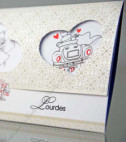 <p>Invitație de nuntă realizată din carton bej, care se pliază în trei pe orizantală. Textul este printat la mijloc, partea de jos conține imagini comice cu mirii, iar partea de sus, care este și coperta invitației, are trei decupaje în formă de inimă prin care se văd imaginile cu mirii. În prețul invitației este inclus plic de culoare roșie.</p>