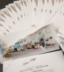 <p>Invitație de nuntă realizată dintr-un carton alb destinat imprimării textului. Acest cartonaș se introduce într-o teacă ce prezintă imaginea a doi miri ce se plimbă în mijlocul unei străzi fumos amenajată.</p>