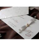 <p>Invitație de nuntă realizată dintr-un carton alb destinat tipăririi textului. Aceasta este accesorizată cu o fundiță albă ce prezintă în mijloc o perlă, oferindu-i invitației o notă de rafinament și eleganță. Invitația este introdusă într-un buzunar ce prezintă un model floral. (Stoc limitat)</p>