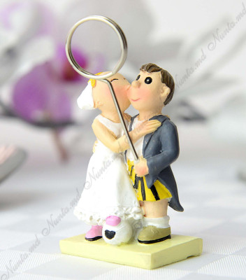 <p>Mărturie de nuntă sub forma unei figurine din ceramică, ce înfaţişează pe cei doi miri. Mirele poartă sacou şi pantaloni scurţi viu coloraţi. Mireasa ţine sub picior o minge. Figurina prezintă un clips metalic ce poate fi folosit ca suport foto sau de card.</p>
